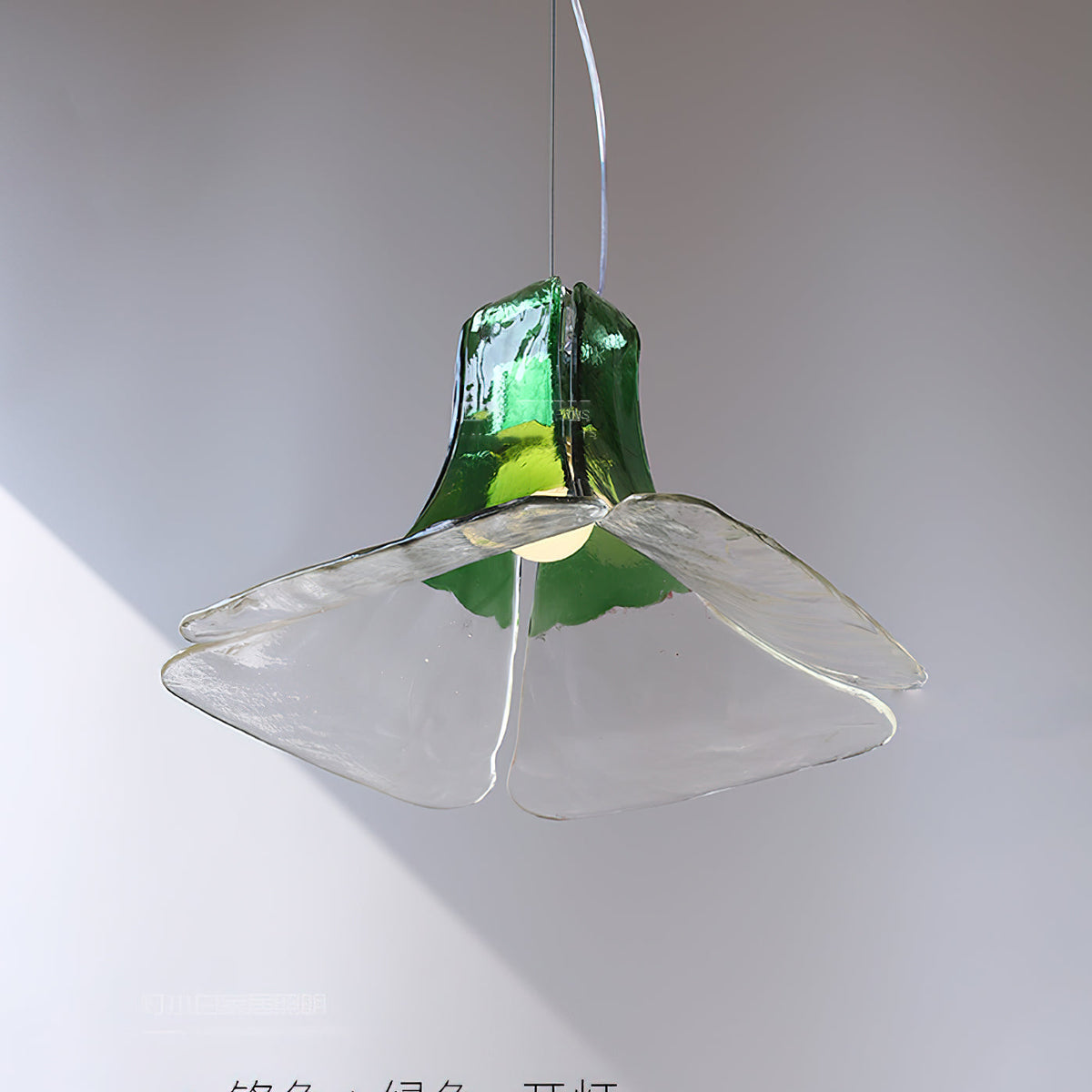 Angled view of the green and clear Carlo Pendant Light against a white wall.