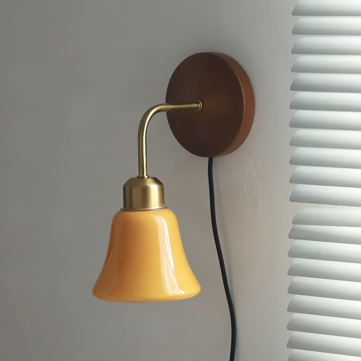 Close-up of the Daphne wall sconce's brushed brass arm and orange glass shade.