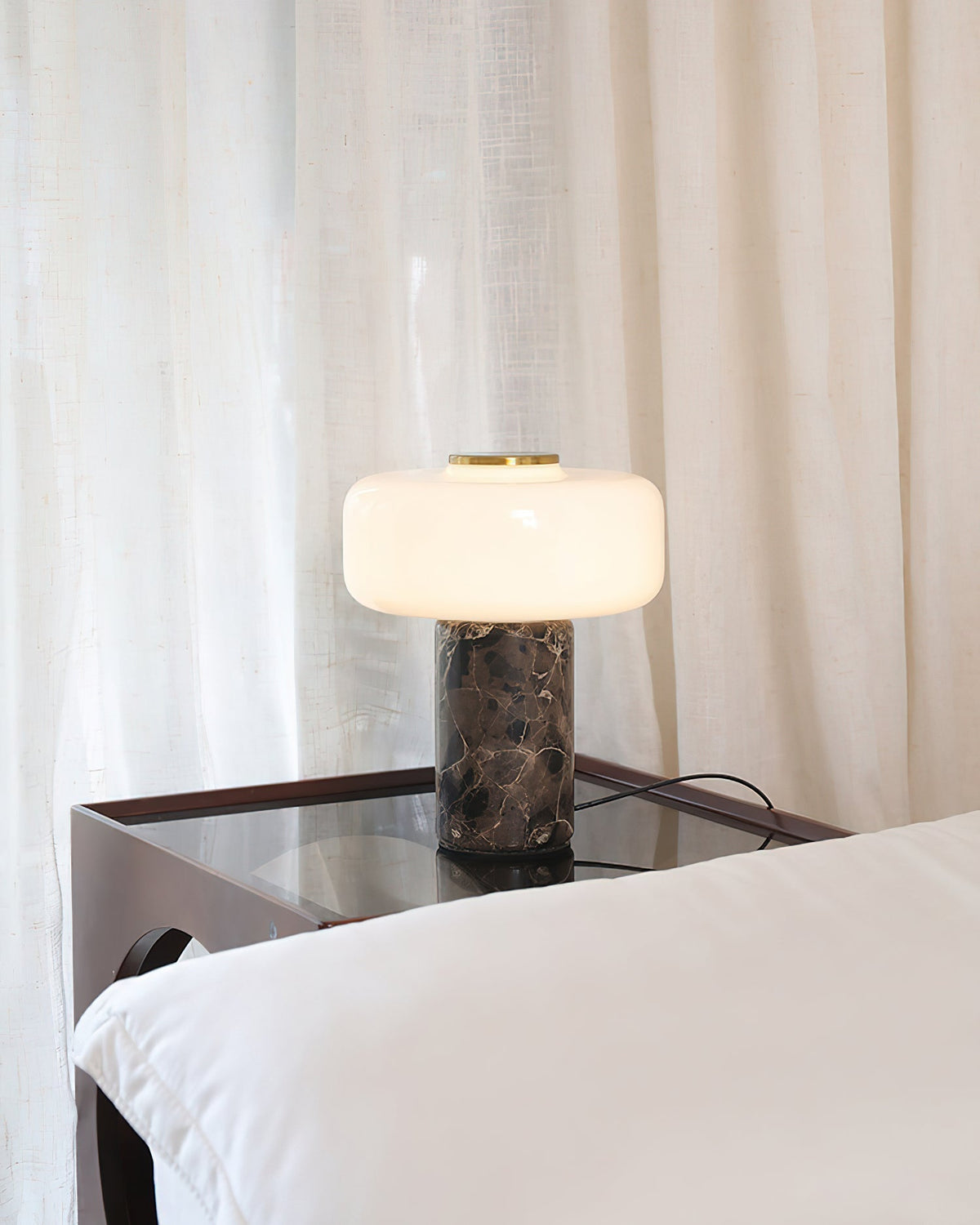 The Lennox Marble Table Lamp shown illuminated in a dark room, highlighting the warm glow.